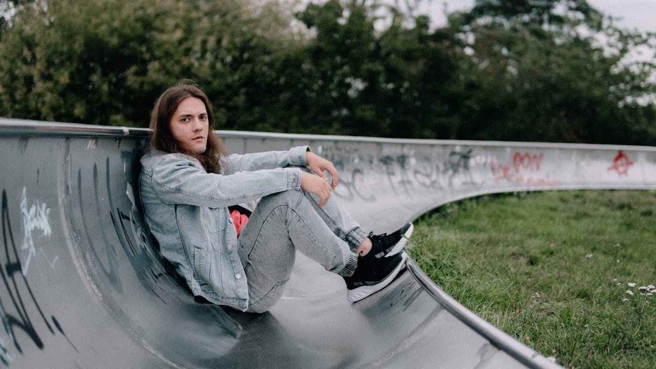 Home Casual young man sitting in a skate park, wearing denim jacket and jeans, in Lodz, Poland.